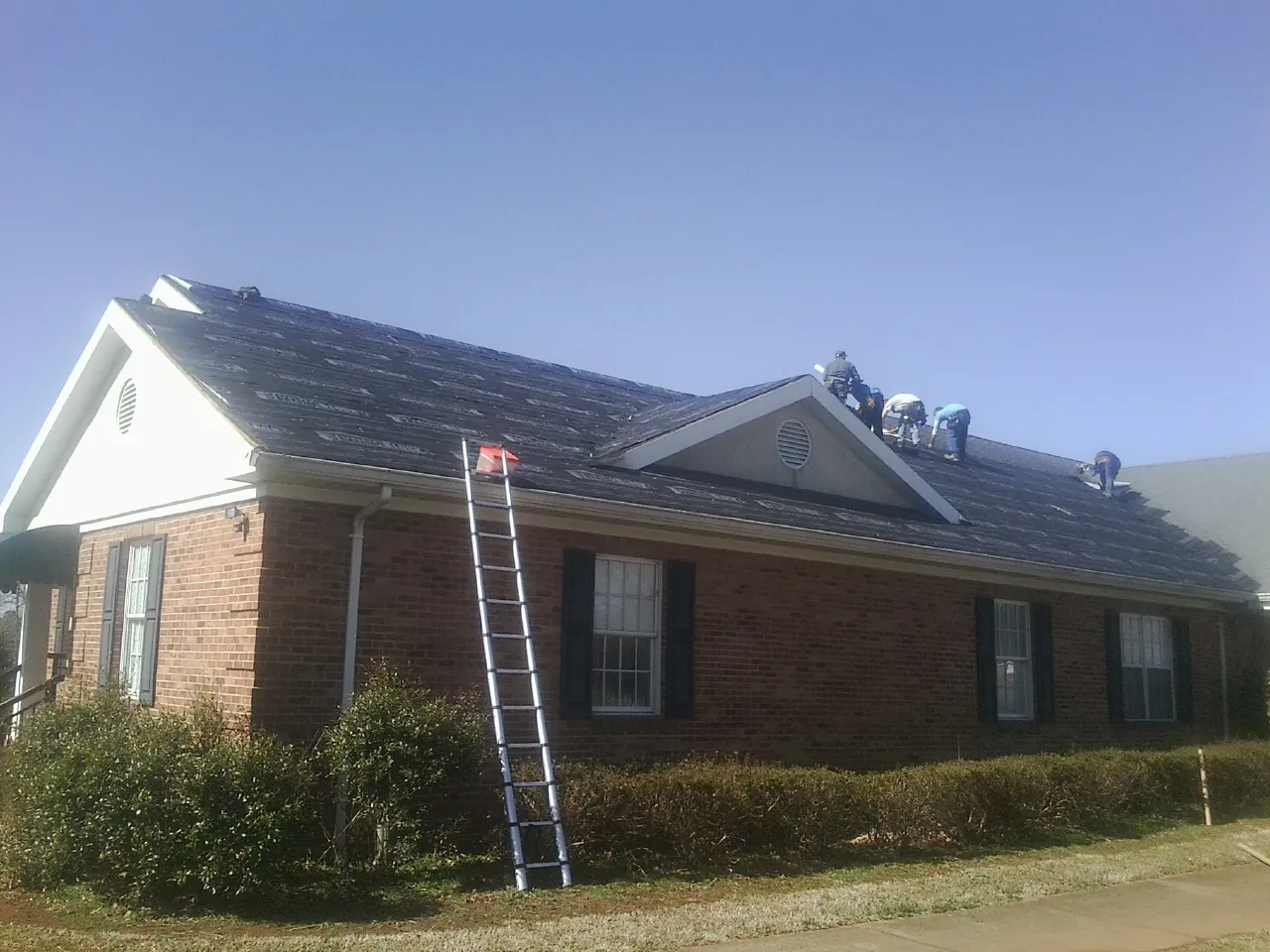 Crew tearing shingles off a brick ranch roof with a ladder set — Metal Roof Repair work by our crew in Rowlesburg