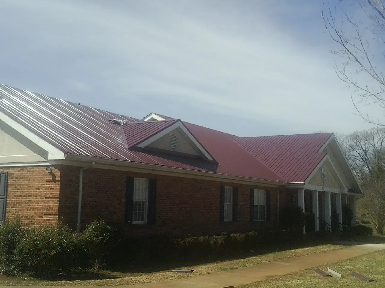 Red metal roof with gabled entries on a long brick building, from a Hail Damage Roof Repair job in Rowlesburg