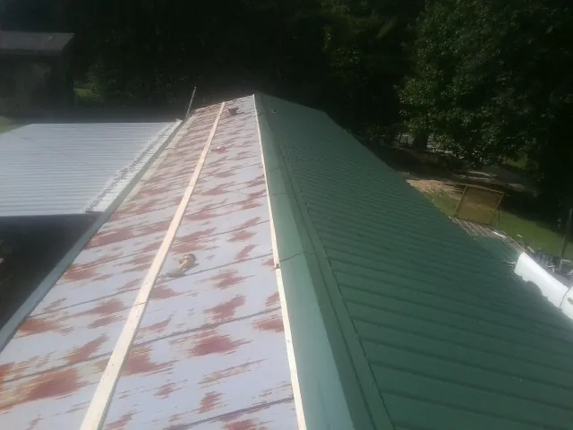 Old rusted panels beside newly installed green metal roofing — Wind Damage Roof Repair by Roofing Brothers in Rowlesburg
