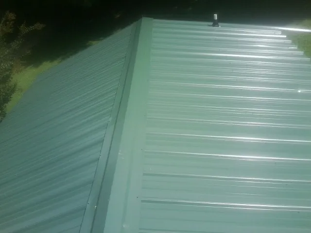 New green metal panels meeting at the ridge of a roof — Flat Roof Repair work by our crew in Rowlesburg