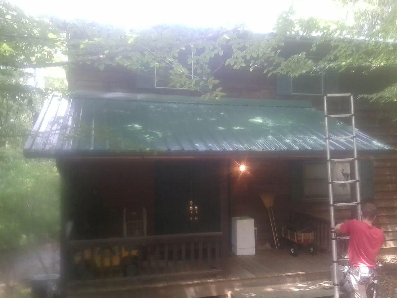 Worker on a ladder at the green porch roof of a wooded cabin in Rowlesburg