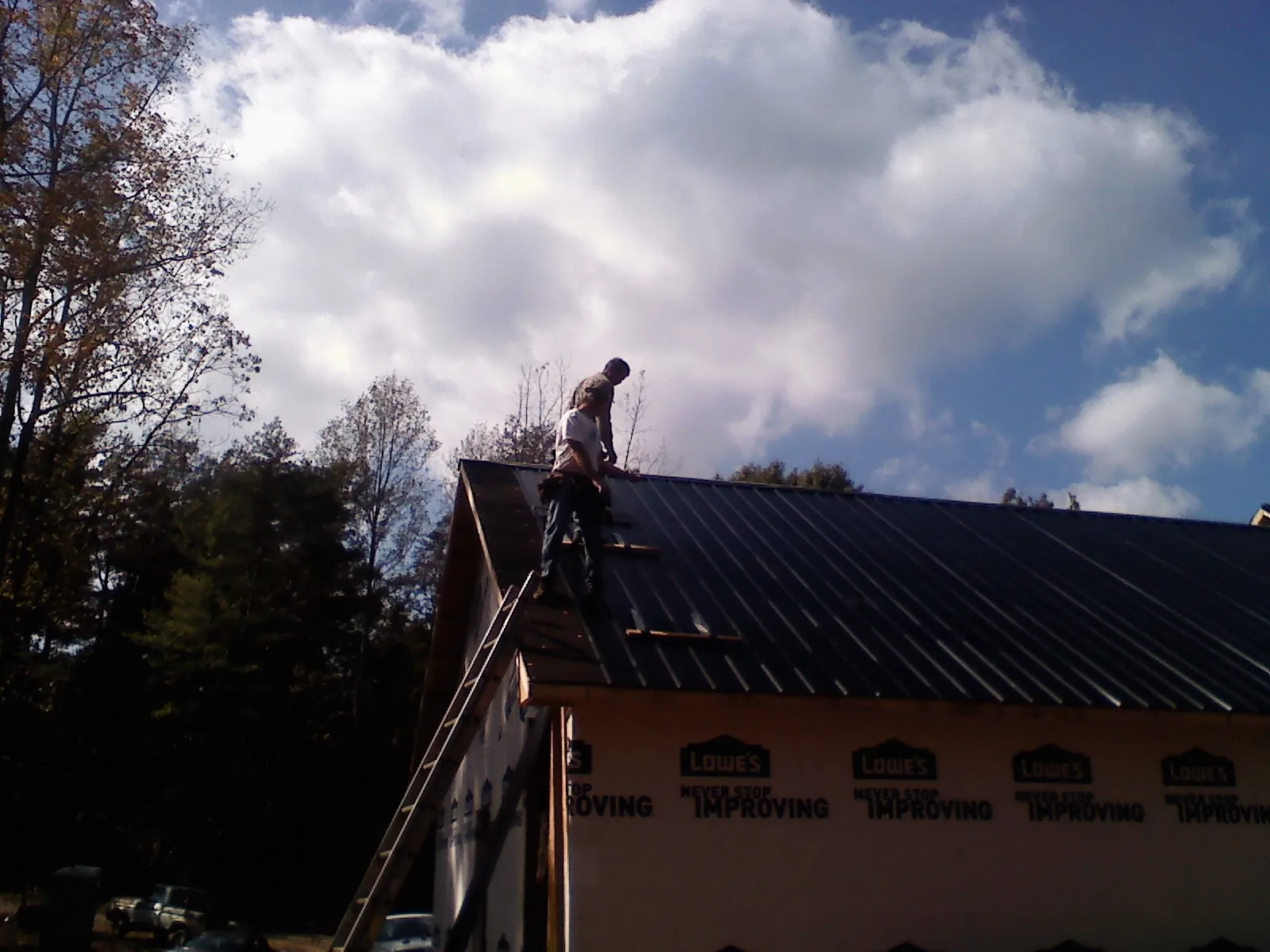 Roofer fastening dark metal panels high against a cloudy sky, from a Roof Inspection job in Rowlesburg