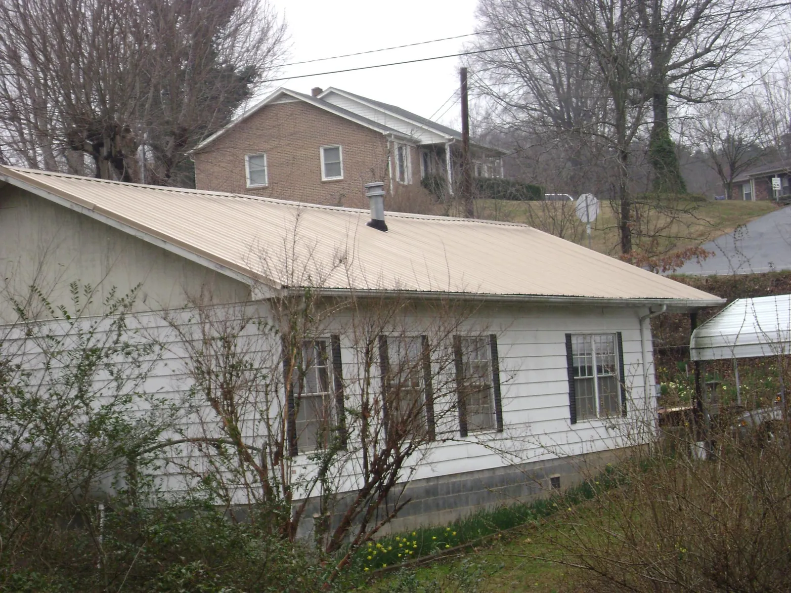 Tan metal roof on a white sided house set into a hillside — Commercial Roofing by Roofing Brothers in Rowlesburg