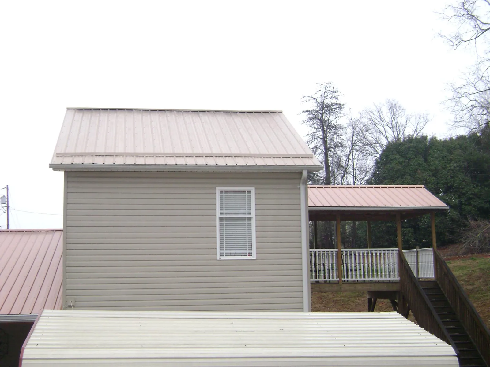 Tan metal roofs on a two story addition and attached porch, from a Roof Replacement job in Rowlesburg